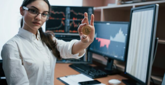 Beautiful woman holding bitcoin in hands while sitting in modern office